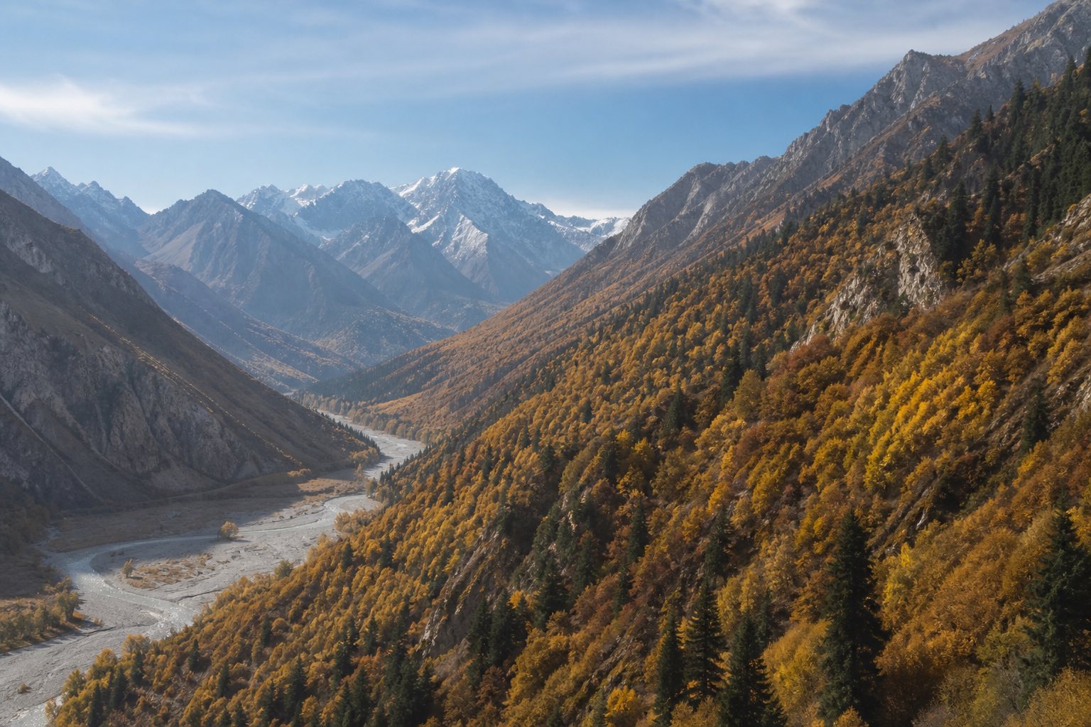 Vallée de montagne aux versants boisés en automne, sommets enneigés au fond.